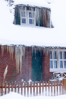 Icicles on a decrative old thatched house covered with snow in a snowstorm in winter,