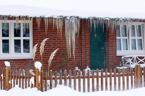 Icicles on a decrative old thatched house covered with snow in snow flurries in winter,