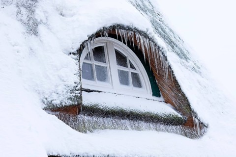 Icicles on a thatched roof covered with snow in front of an icy window in winter,