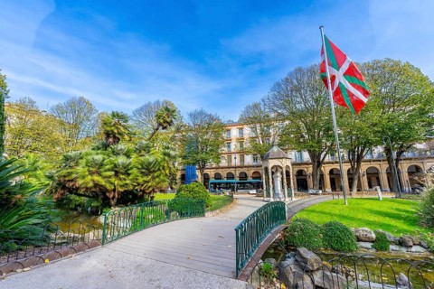 Gipuzkoa plaza park showing lush greenery, a pond with a small bridge, historic buildings, and the