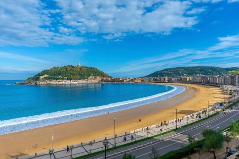 La concha beach curving along the bay of san sebastian city, with people walking on the sand and