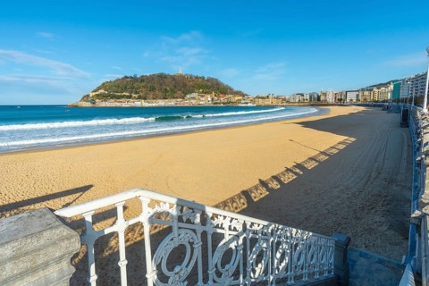 La concha beach view with its iconic promenade railing, golden sand and the city of san sebastian