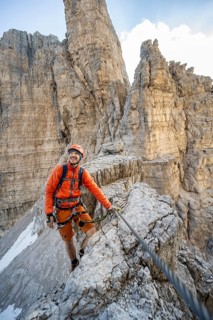 Mountaineer climbs on an exposed rock in the secured via ferrata Bocciere Centrale, Brenta