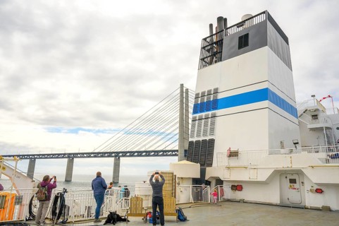 Passengers on a ship with a view of the Øresund Bridge, a ferry under a massive bridge structure of