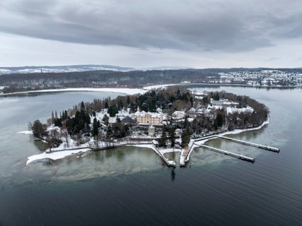 The wintry and snowy Mainau island in Lake Constance with the pier and the baroque Mainau Castle,
