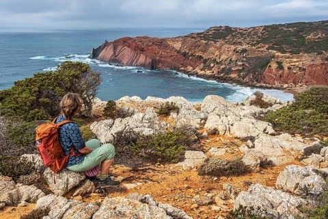 Hiking woman takes a break, view over cliff, Fishermens Trail, Rosa Vicentina, western Algarve just