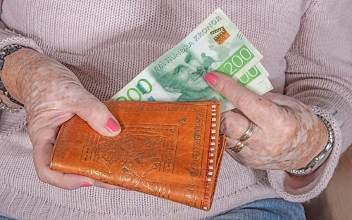 An elderly woman's hands take out Swedish banknotes from a wallet