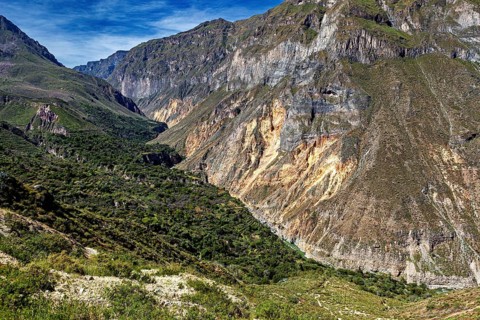 Wide valley surrounded by steep rock cliffs under blue skies, the landscape of the Colca Canyon in