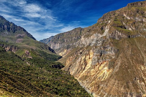 Impressive rock cliffs stretch across a green valley, the landscape of the Colca Canyon in the Aden