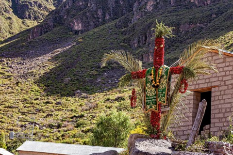 A scarecrow decorated with traditional costumes stands in a sunny mountain landscape next to a