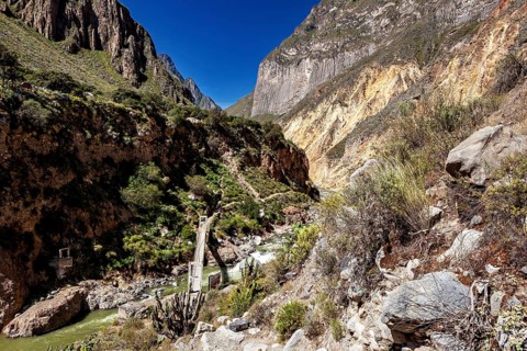Suspension bridge spans river in deeply cut gorge with steep rocks, the landscape of Colca Canyon