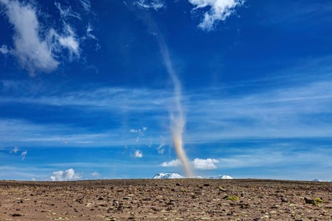 A tornado swirls dust over a dry landscape under a clear blue sky with few clouds, dust devils in