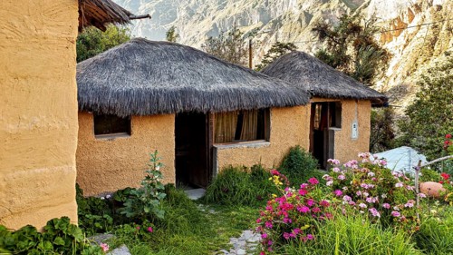 Rustic clay huts with thatched roofs in a blooming, mountainous landscape under bright sunshine,