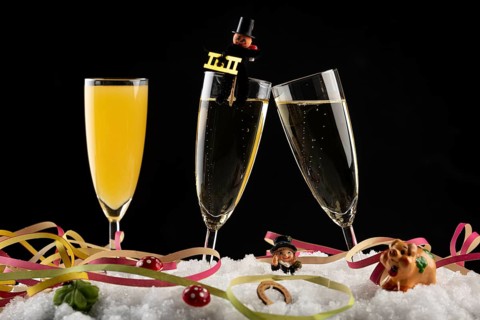 Three champagne glasses with lucky charms for the New Year and streamers in the snow