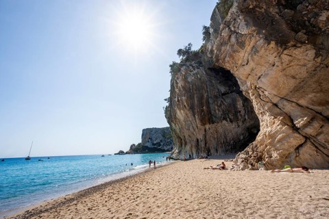 Sandy beach beach and steep cliffs with caves at Cala Luna, Golfo di Orosei, Baunei, Sardinia,