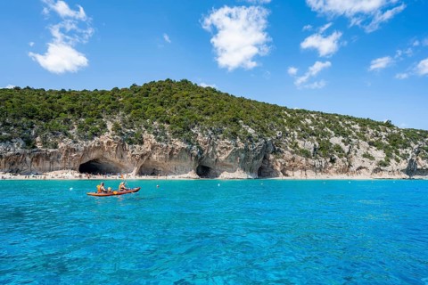 Kayakers in clear blue water, picturesque rocky coast, cliffs and Cala Luna beach, Golfo di Orosei,