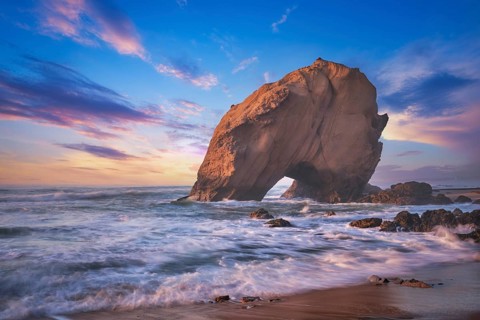 Penedo do Guincho, a large boulder rock arch at Praia da Santa Cruz, Portugal, with ocean waves and