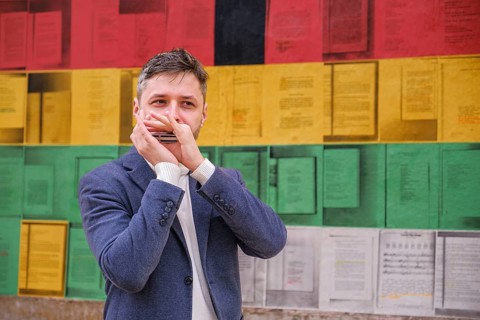 Man musician in a blue blazer and white sweater playing blues on a harmonica with eyes closed,