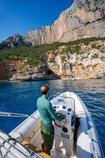 Young man rides a motorboat along the picturesque rocky coast, cliffs and blue sea, Golfo di