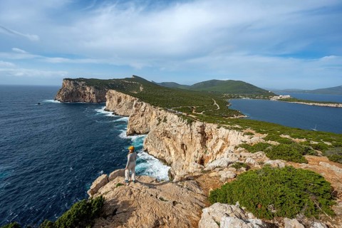 Tourist enjoying the view of steep cliffs by the sea, coastal landscape, cliffs on the Capo Caccia