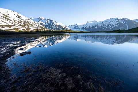 Mountain peaks with Portage Glacier glacier and snow reflected in Divide Lake mountain lake in