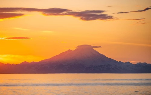 View of Cook Inlet on white mountain peaks of Mount Redoubt at sunset, picturesque golden light of