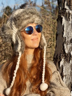 Slender pretty woman with fur hat and pompoms, red hair and warm winter colors between birch forest