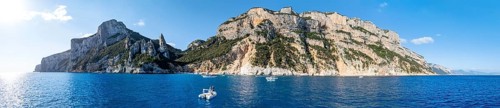 Couple on motorboat off picturesque rocky coast, cliffs with L'Aguglia pinnacle, blue sea and Cala