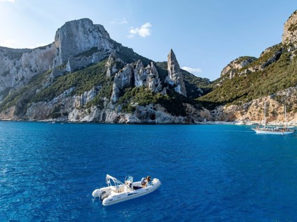 Motor boat off picturesque rocky coast, cliffs with L'Aguglia pinnacle, blue sea and Cala Goloritzé