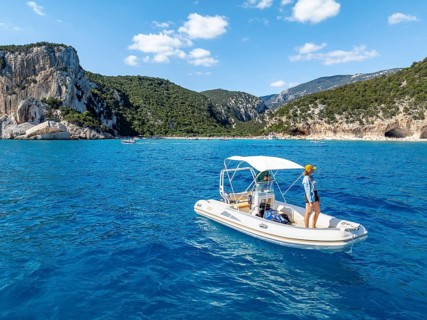 Motor boat off picturesque rocky coast, cliffs and Cala Luna beach, aerial view, Golfo di Orosei,