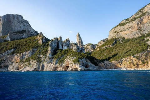 Picturesque rocky coast, cliffs with caves in the morning light, L'Aguglia rock peak, blue sea and