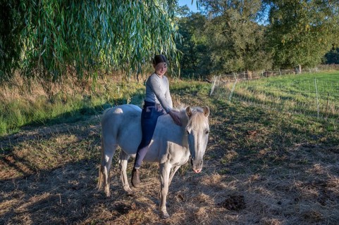 Young girl sitting on her white mare under a willow (Salix), Othenstorf, Mecklenburg-Western