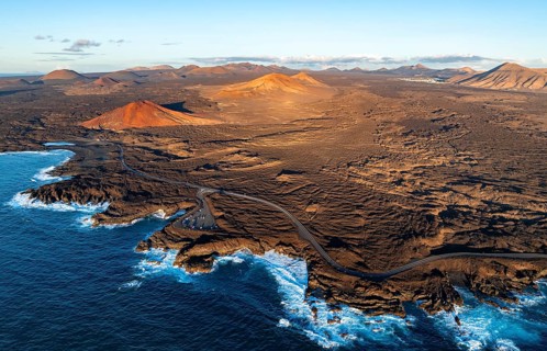 Coast with lava fields, volcanic landscape near Los Hervideros with red volcano Montaña Bermeja, in