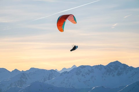 Paragliders flying over snowy mountain peaks in winter in evening light, Kitzbühel Alps, Tyrol,