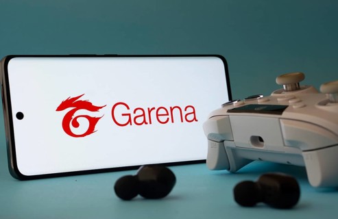 Dhaka, Bangladesh- 23 Mar 2025: A smartphone with a Garena icon next to a controller and earbuds on