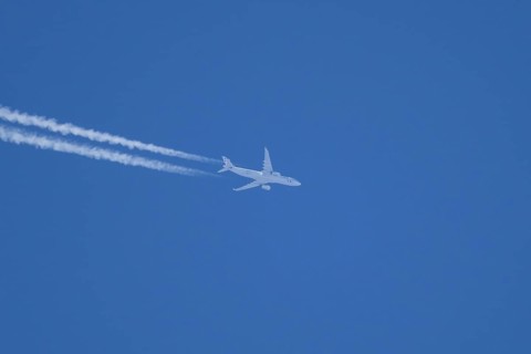 Jet passenger aircraft flying in a blue sky with contrails or vapour trails behind, England, United