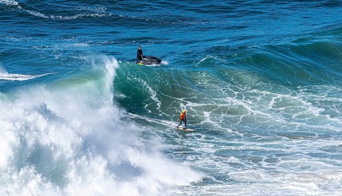 Surfers with their jet ski pilots in the Atlantic waves below Farol de Nazaré, Forte São Miguel,