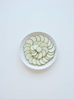 Thinly sliced zucchini arranged on a white plate, forming a visually appealing pattern of