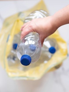 Close-up of hand putting plastic bottle into yellow recycling bag, promoting environmental
