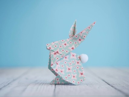 Floral origami easter bunny standing on a white wooden table with a light blue background
