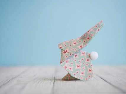 Floral origami easter bunny standing on a wooden table against a blue background