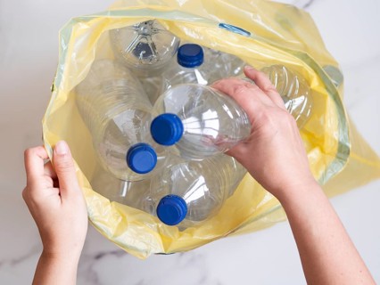 Woman putting used plastic bottles into yellow garbage bag, top view, recycling concept