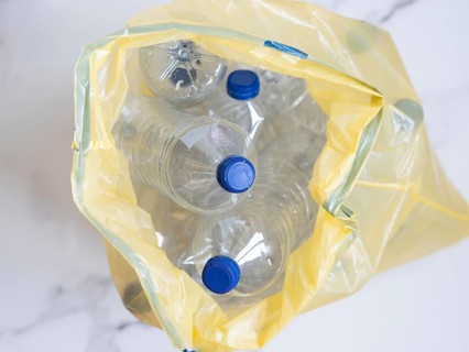 Plastic bottles with blue caps collected in yellow trash bag ready for recycling
