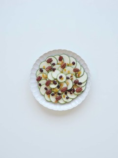 Sliced zucchini arranged on a white plate, creating a carpaccio with raisins and pecans, forming a