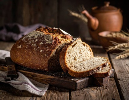 Rustic loaf of whole grain bread, fresh baked, close up of bread on dark wooden table, golden rust,