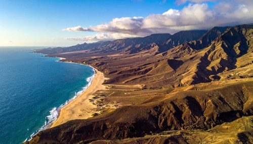 Desert landscape converges with ocean along a rugged coastal area, shore break at cliffs, blue