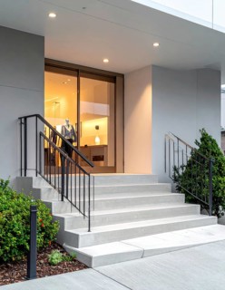 Modern building entrance with stairs, glass facade, and plants in warm evening light, empty