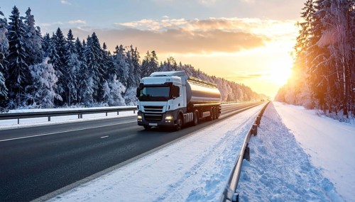 Petrol cargo truck lorry tanker driving on highway hauling oil products at sunrise, wide snowy