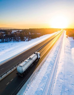 Petrol cargo truck lorry tanker driving on highway hauling oil products at sunrise, wide snowy
