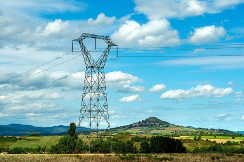 High voltage power lines against a bright blue sky with scattered clouds, Puy de Dome, Auvergne